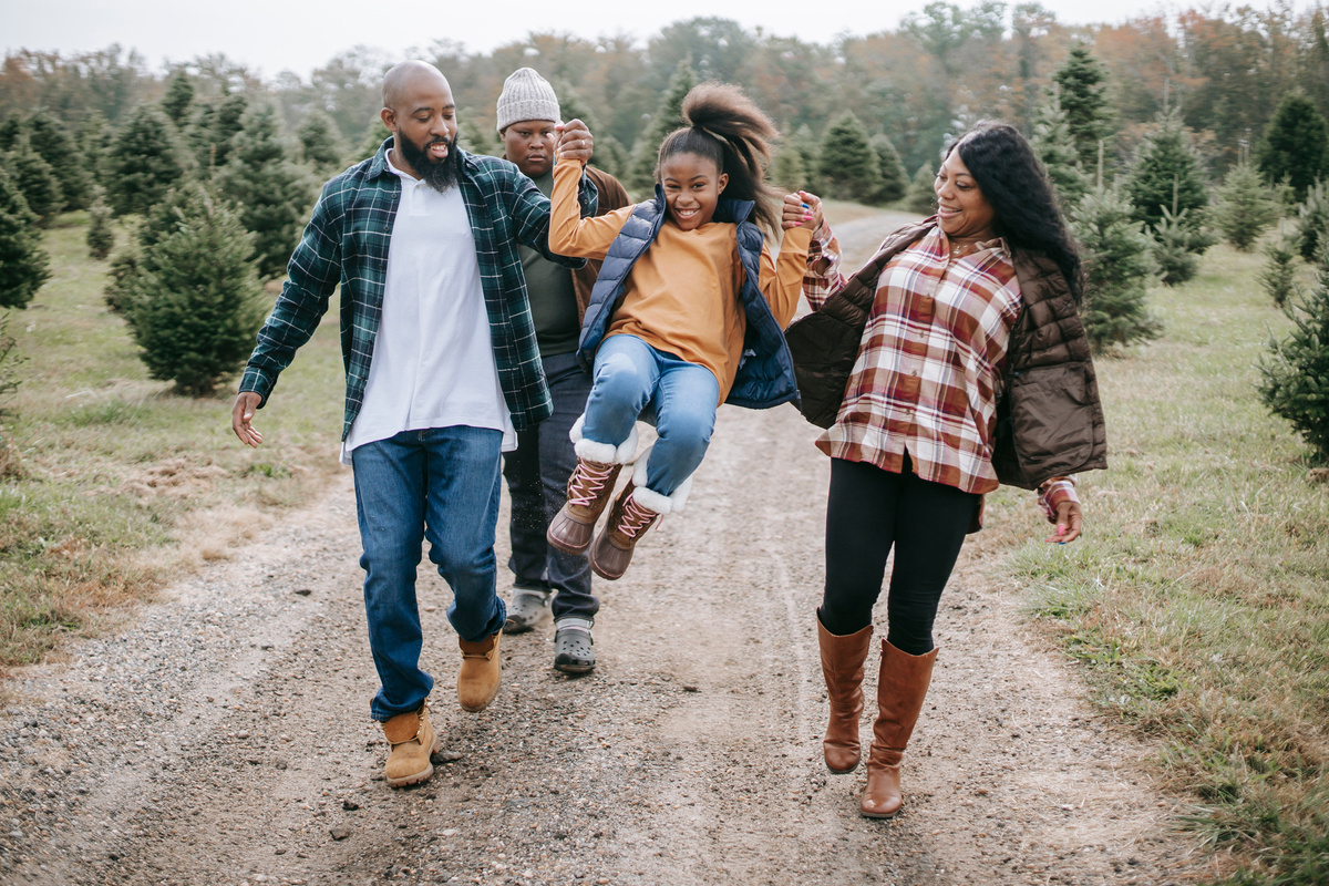 Ethnic parents raising cheerful girl on tree farm roadway