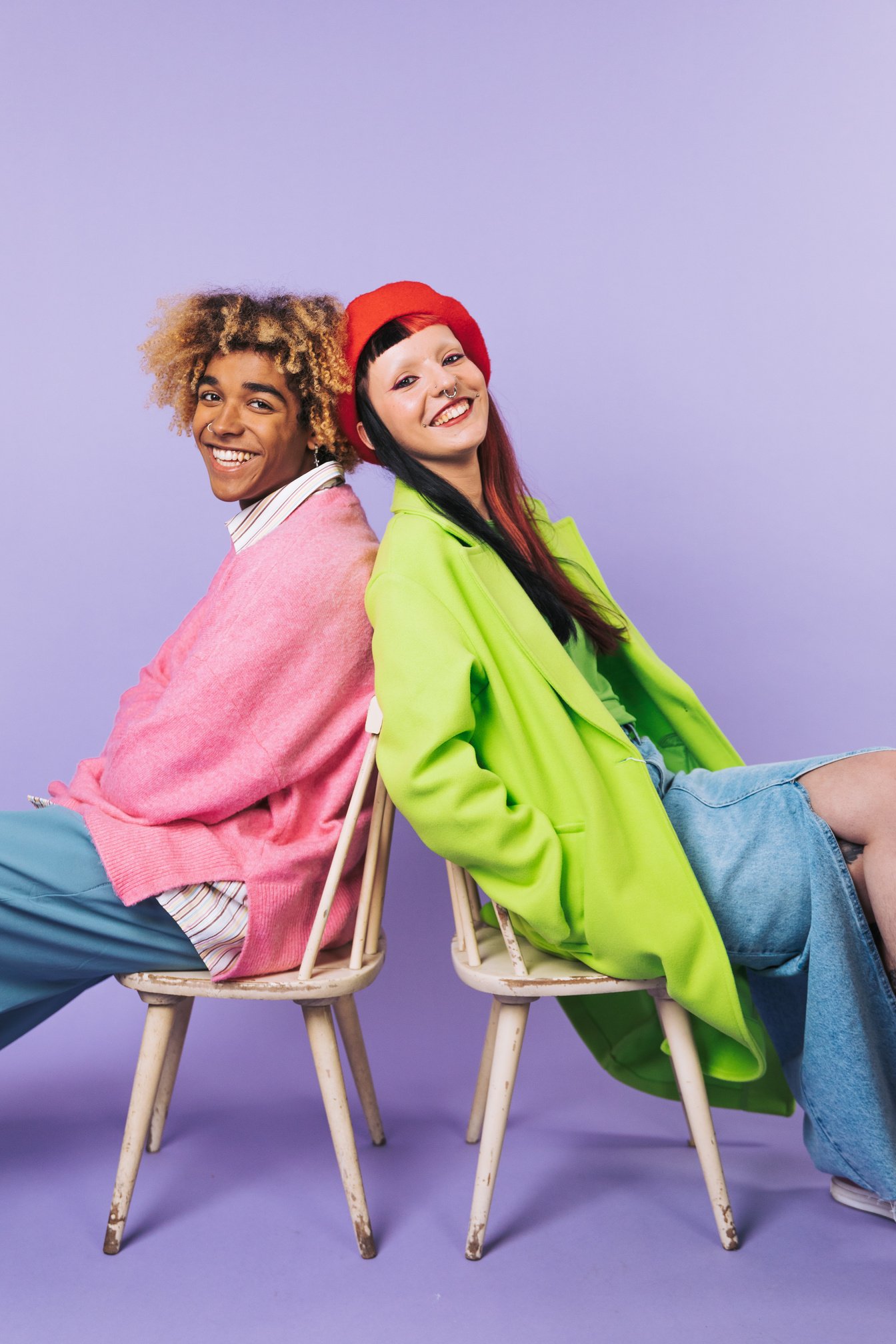 two people smiling at the camera in front of a purple background